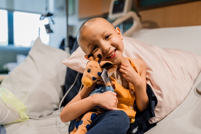 A child holding a stuffed giraffe smiling on their hospital bed