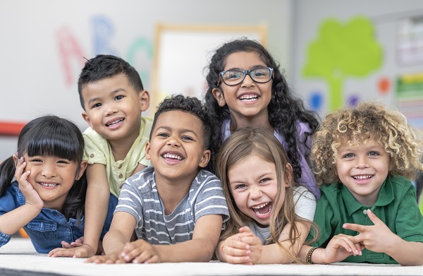 Six young children smiling together in a classroom