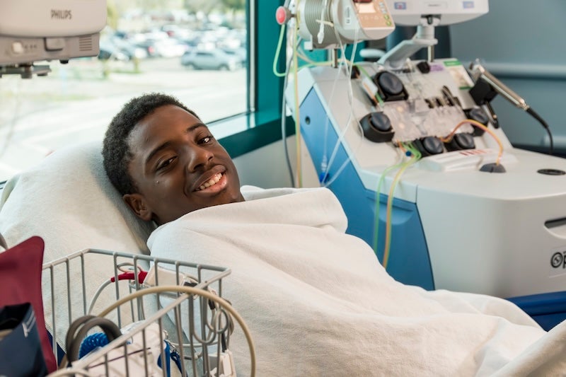 A young man resting in a hospital bed with a blanket up to his neck.