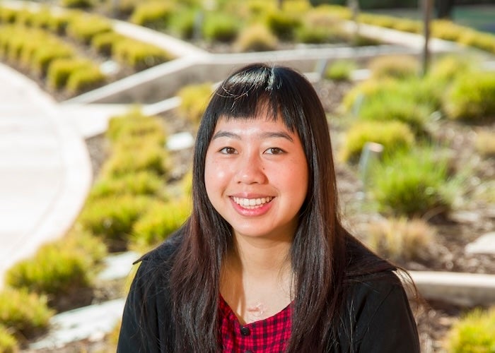 A woman with long hair sitting at a wooden table smiling