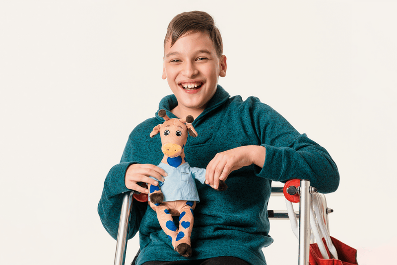 A young boy smiles as he holds a George the Giraffe plush toy