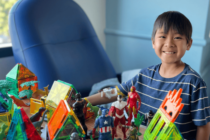 Jeremy smiles next to his superhero toys