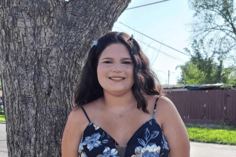 A teenage girl smiles as she stands next to a tree