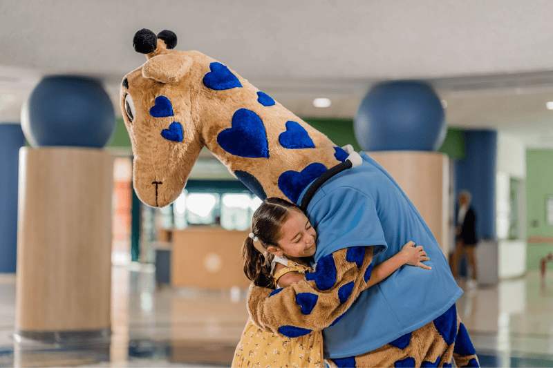 A small girl hugs Valley Children's mascot, George the Giraffe