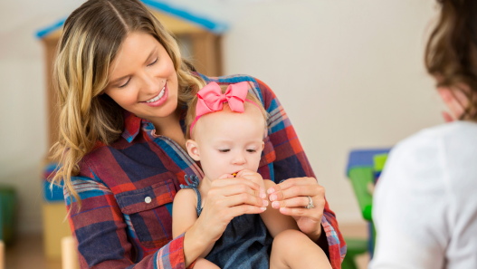 Mom holding baby and teaching her ASL (American Sign Language) sign for more