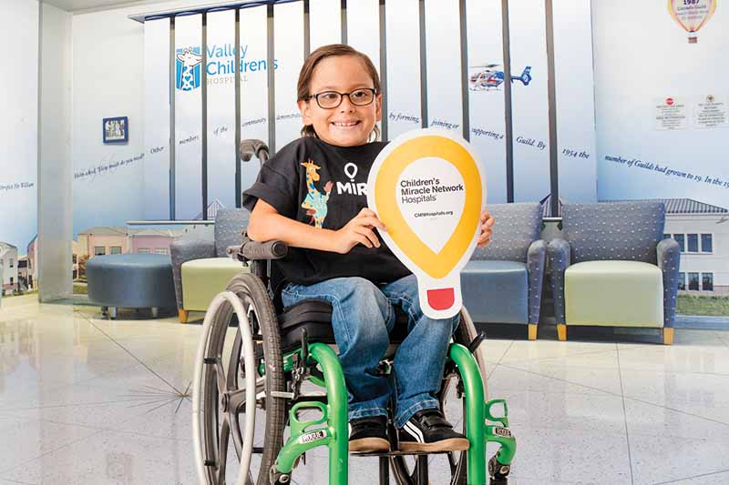 Child in a wheelchair holds a CMN balloon